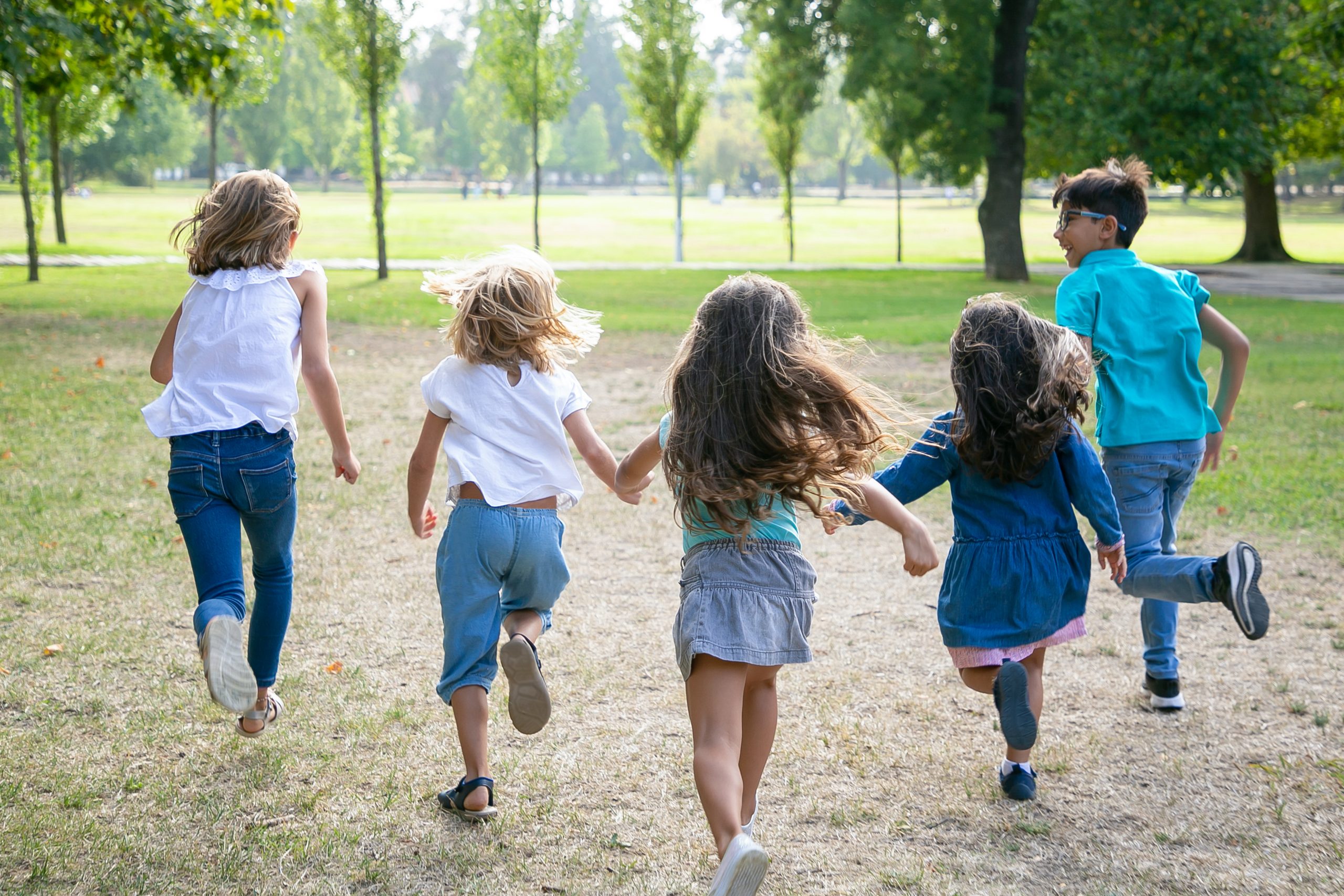 Groupe d'enfants courant ensemble sur l'herbe, dans un parc. Vue de dos, en pied. Concept d'activité de plein air pour enfants.